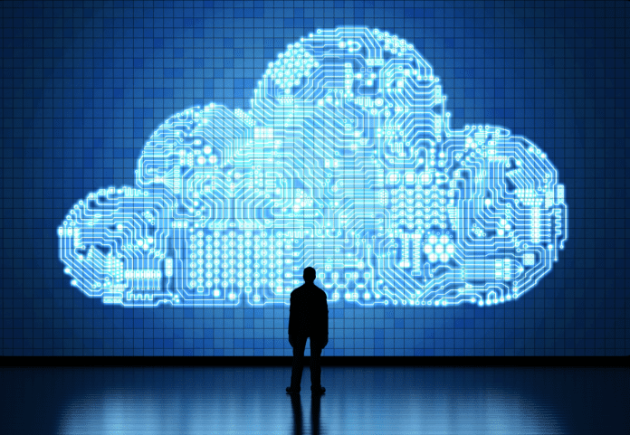 Man standing in front of a giant screen showing an enlarged cloud icon formed from circuit patterns.